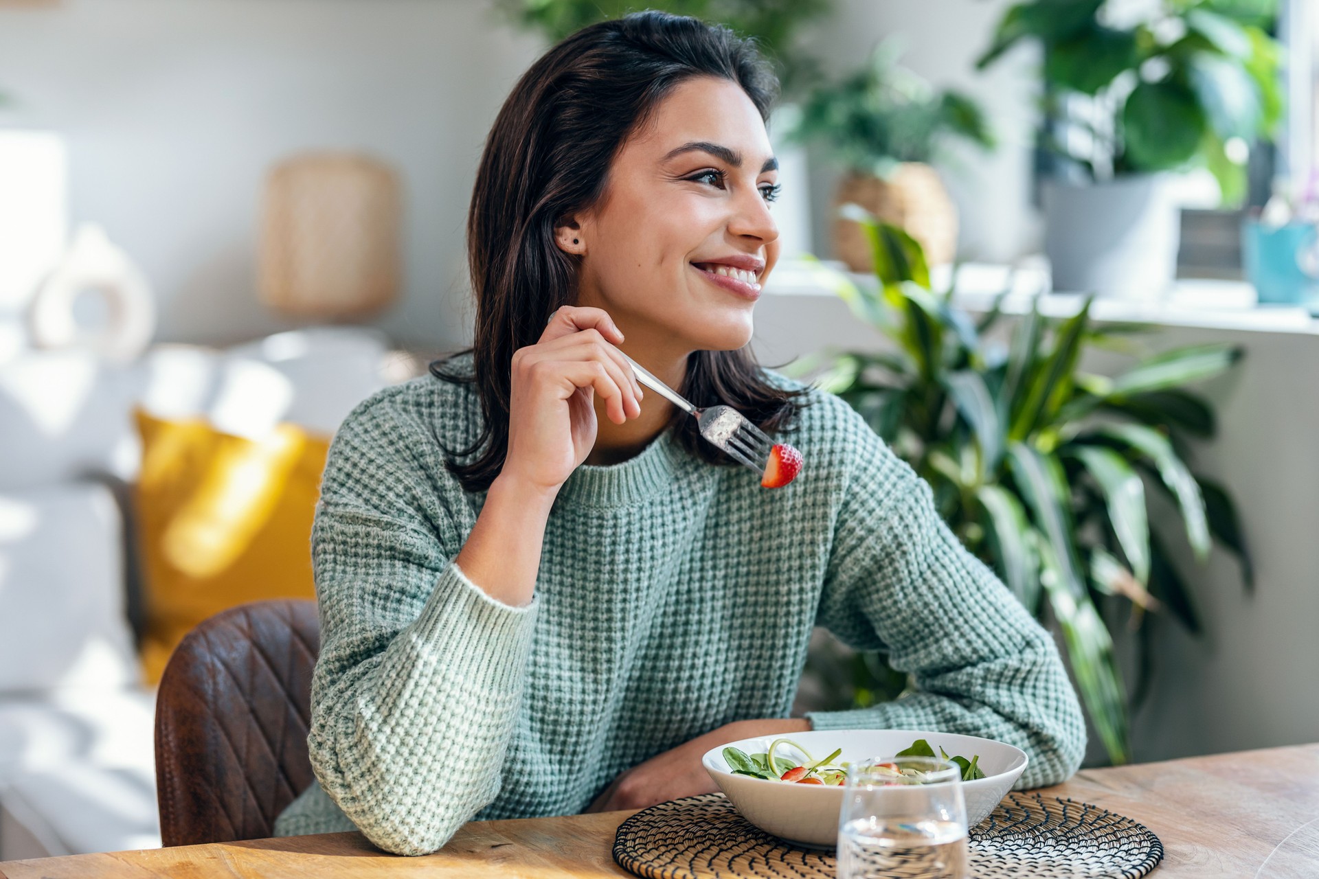 Hermosa mujer sonriente comiendo ensalada saludable en casa.